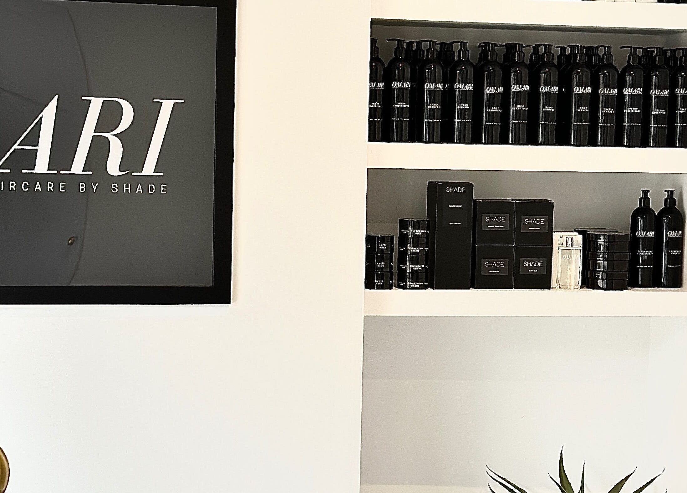 Display of beauty products at SHADE ANDOVER, Andover, England, GB, showcasing sleek black bottles on white shelves.