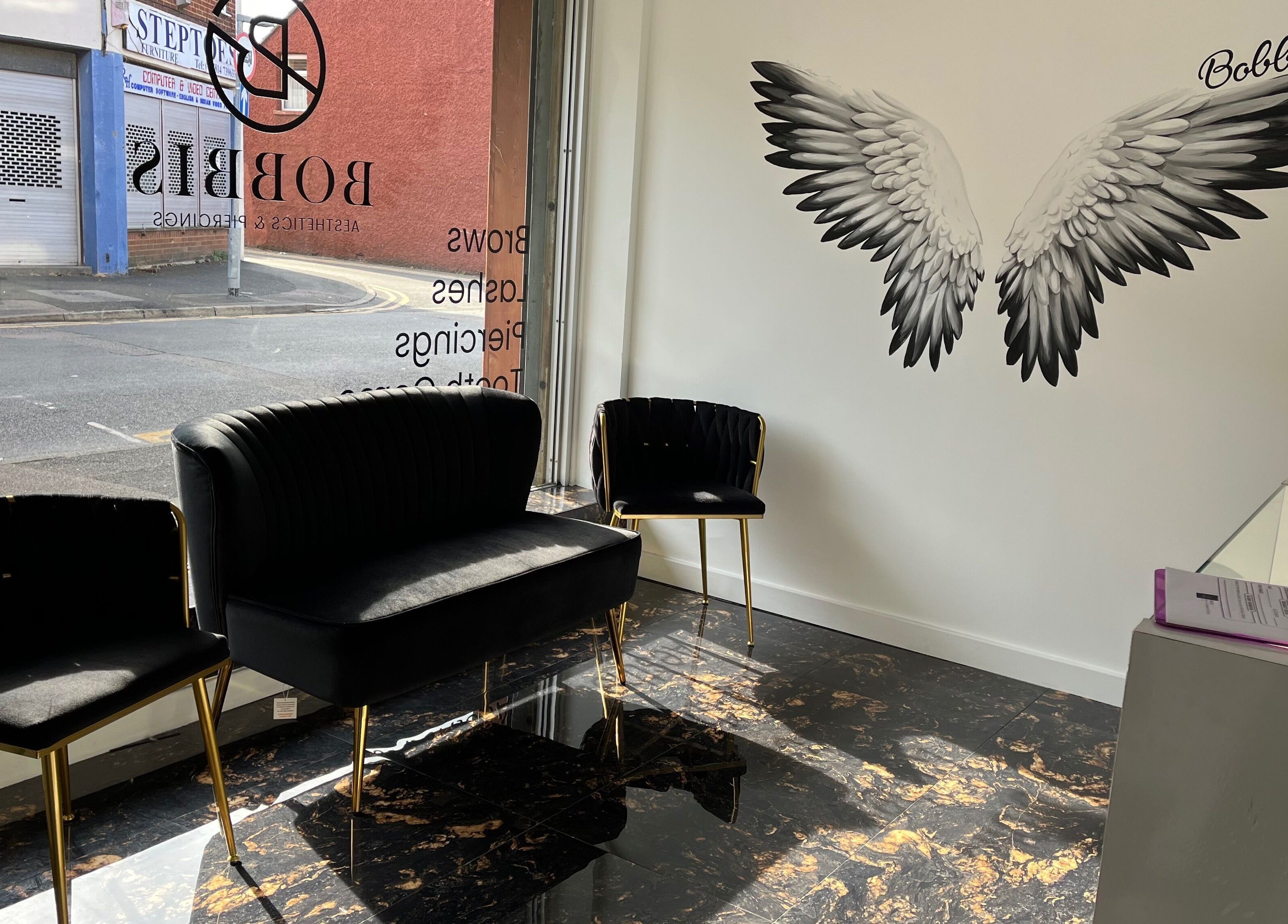 Chic waiting area at Bobbi's Aesthetics & Piercing, Bletchley, England, GB with black chairs and angel wings mural.