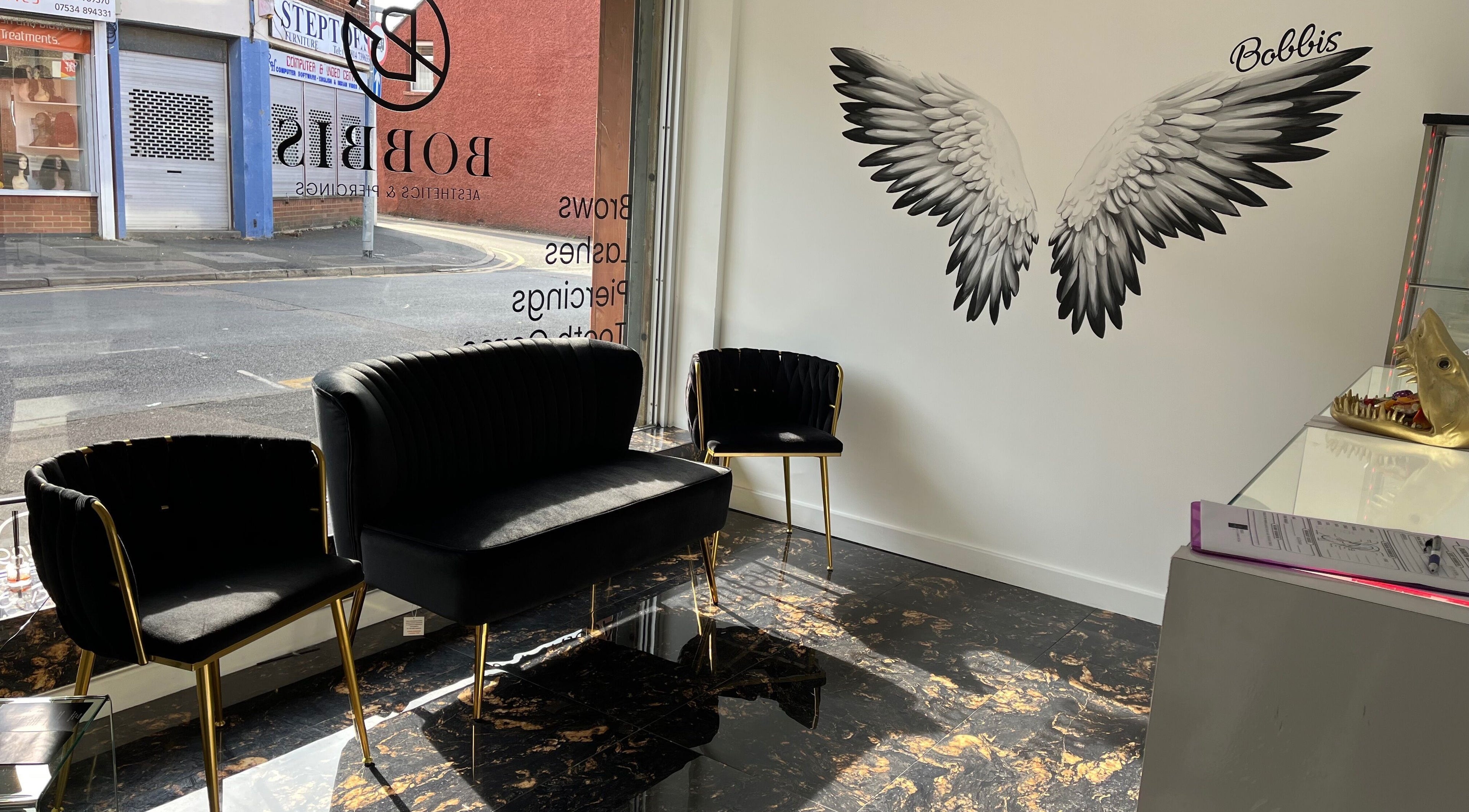 Chic waiting area at Bobbi's Aesthetics & Piercing, Bletchley, England, GB with black chairs and angel wings mural.