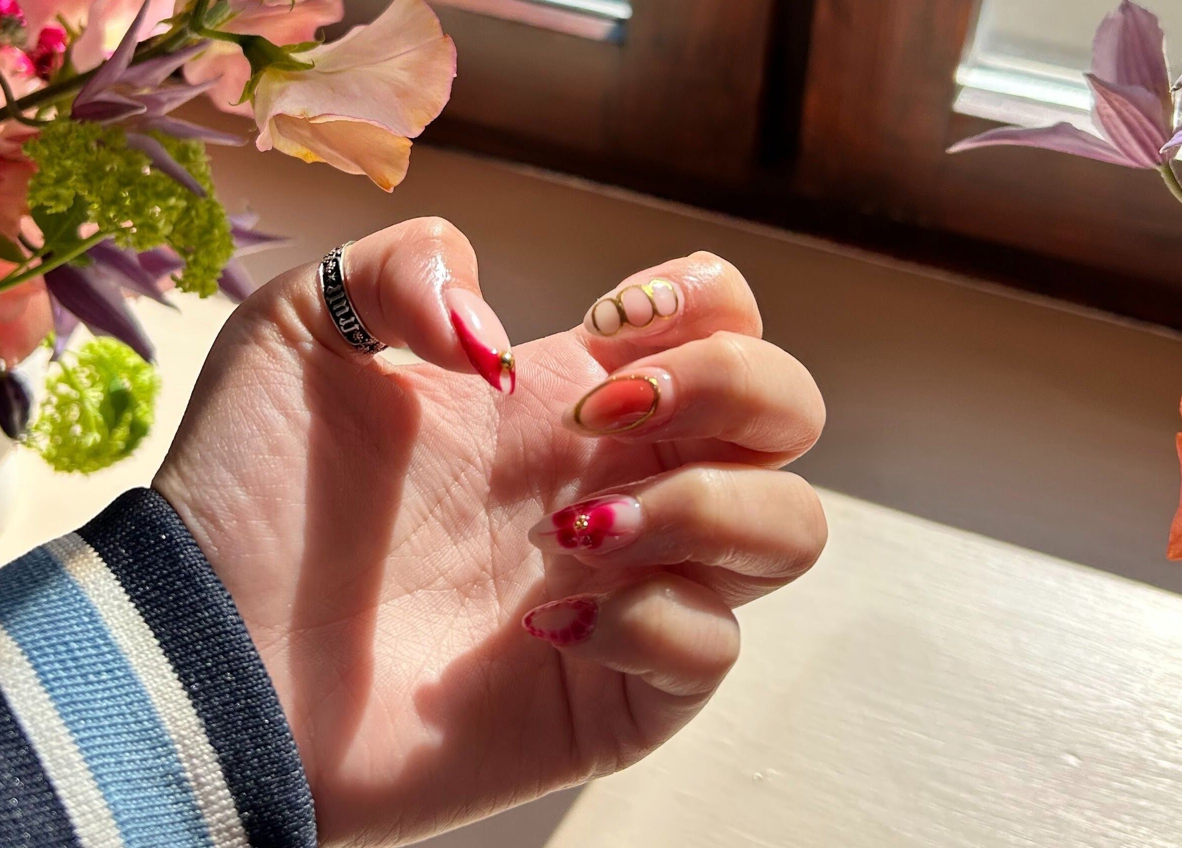 Elegant floral nail art at Claws and Pause in Edinburgh, Scotland, GB, with vibrant blossoms in the background.