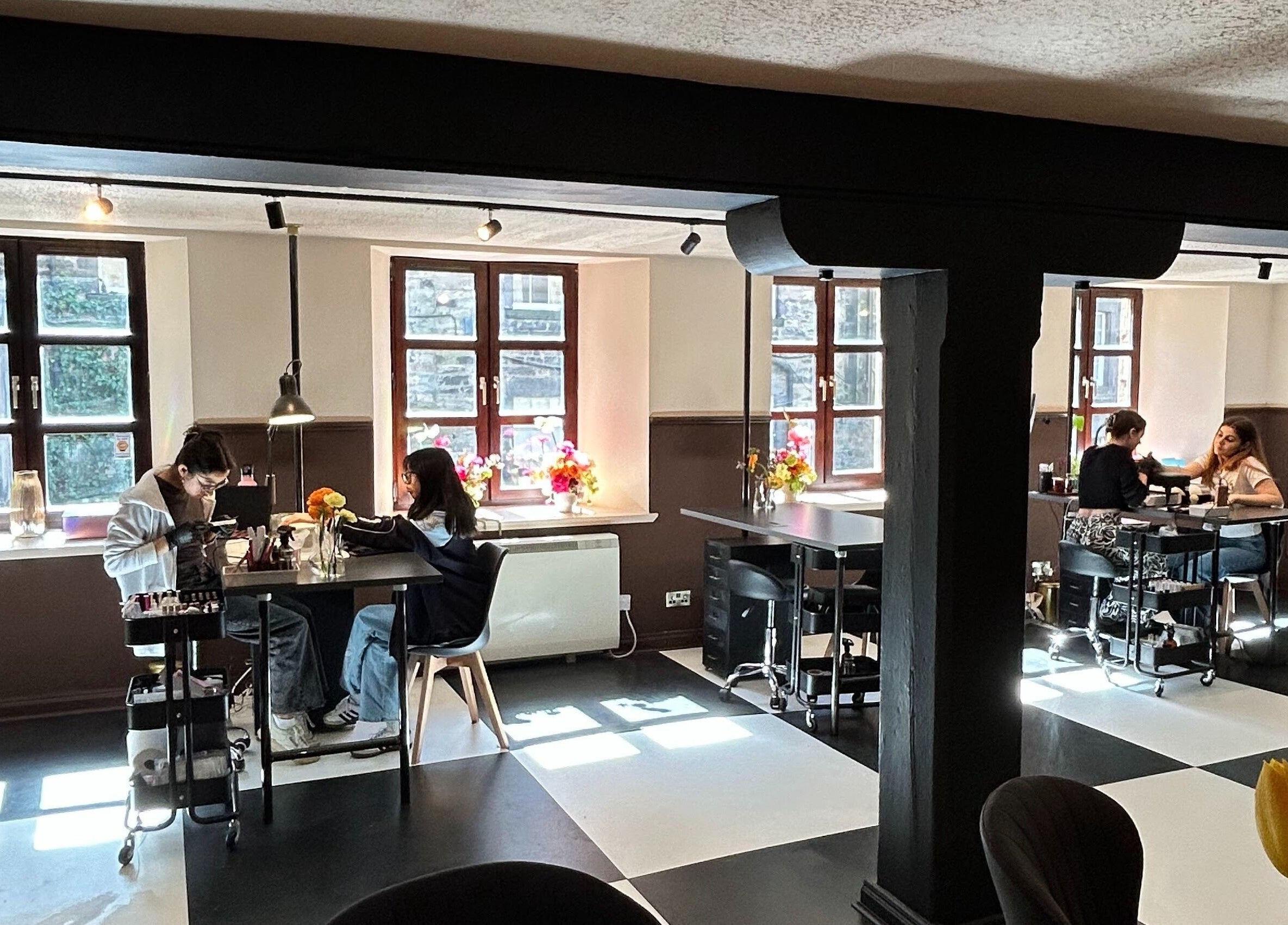 Clients enjoying manicures at Claws and Pause, Edinburgh, Scotland, GB, with vibrant flowers by sunlit windows.