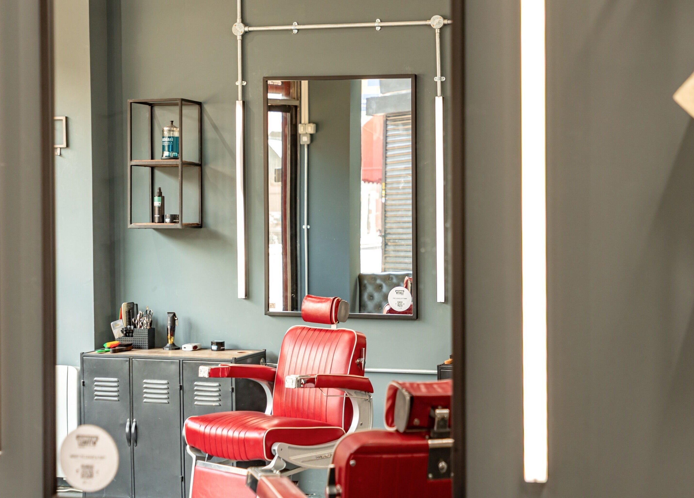 Chic red barber chair in Curfew Grooming Brixton, London, England, GB. Modern grooming space with mirror and shelves.
