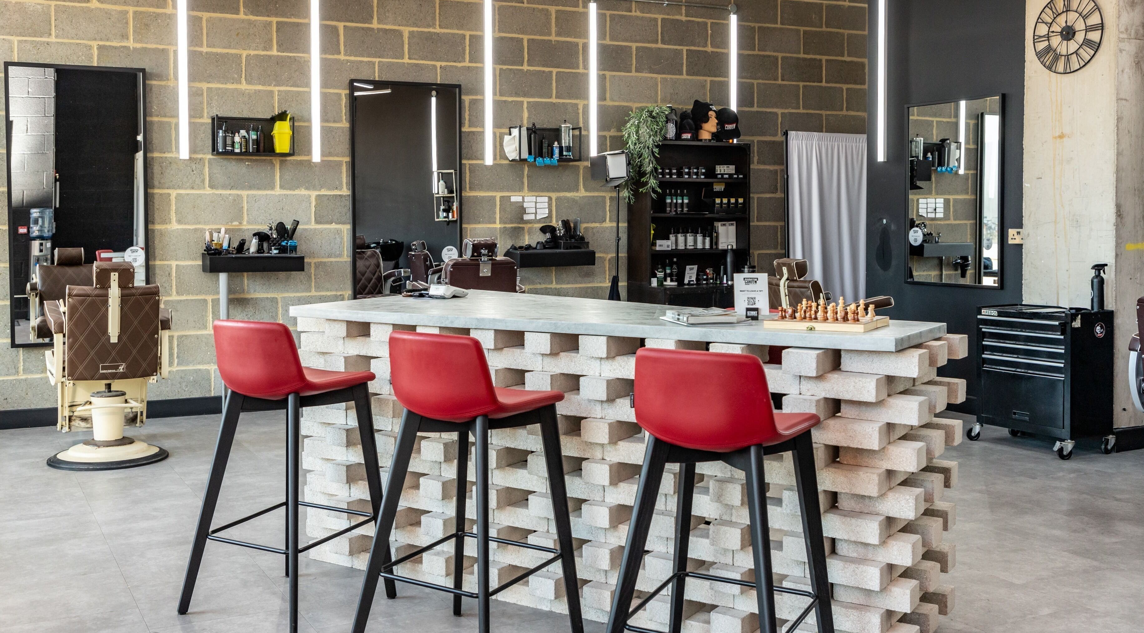 Interior of Curfew Grooming Hackney Wick in London, England featuring modern decor and red chairs.