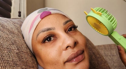 Woman with styled lashes relaxing at The Lash Shack, Randburg, Gauteng, ZA, holding a small fan.