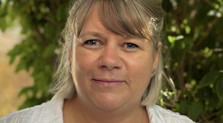 Portrait of a relaxed, smiling woman at Relax & Glow, Swindon, England, GB, surrounded by lush greenery.
