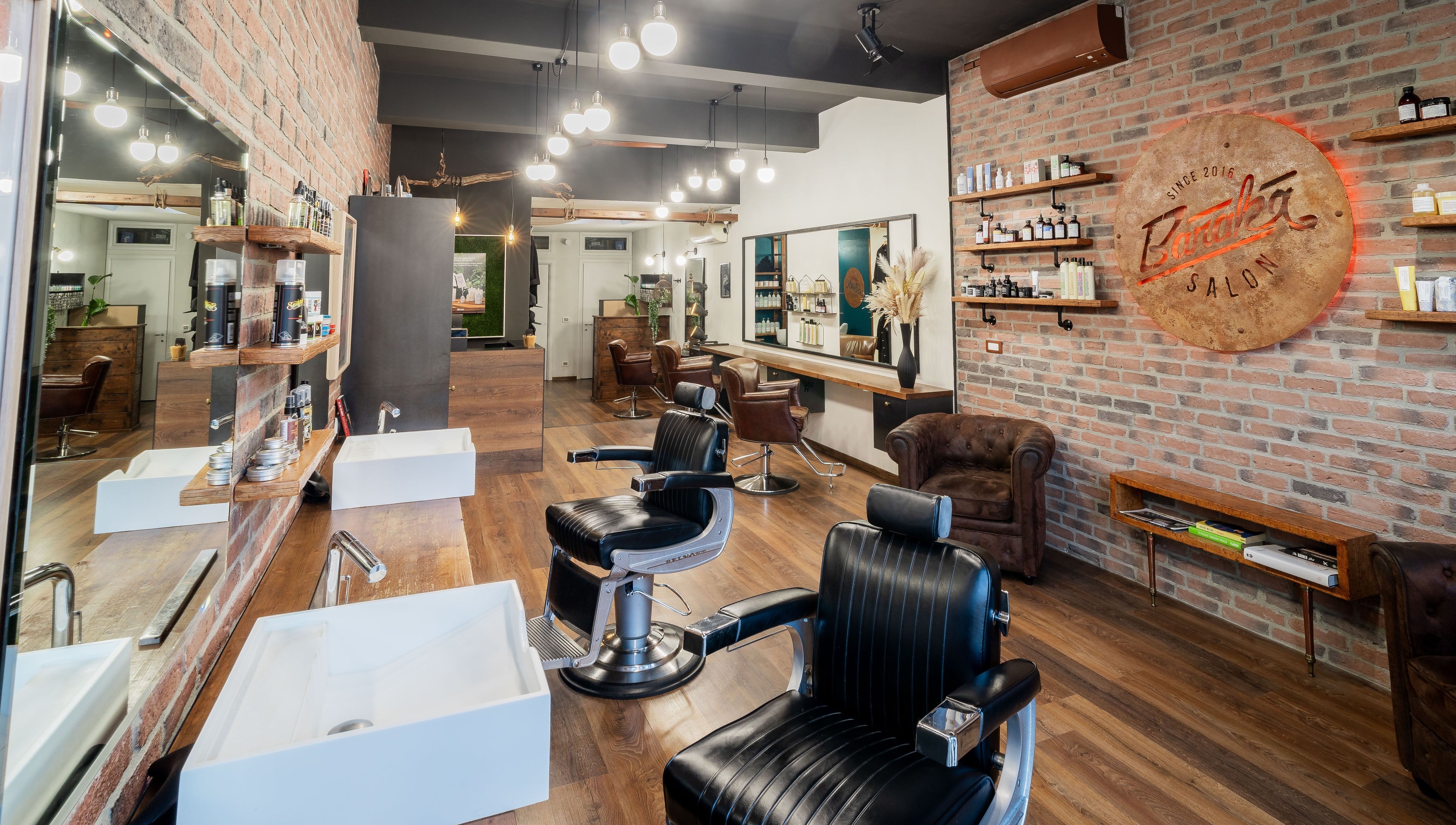 Interno moderno di Baraka Salon a Este, Veneto, IT con sedie da barbiere nere e pareti in mattoni.