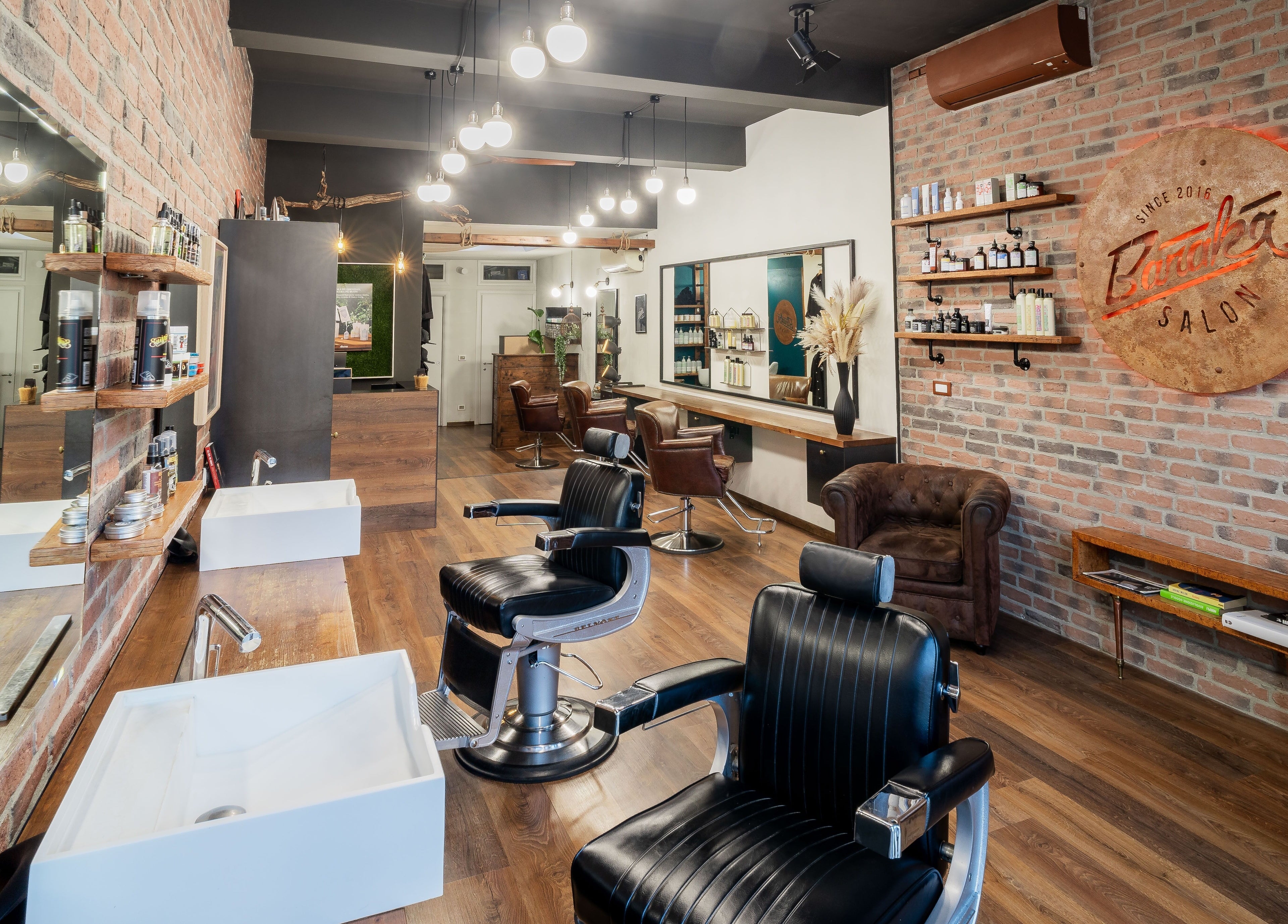 Interno moderno di Baraka Salon a Este, Veneto, IT con sedie da barbiere nere e pareti in mattoni.