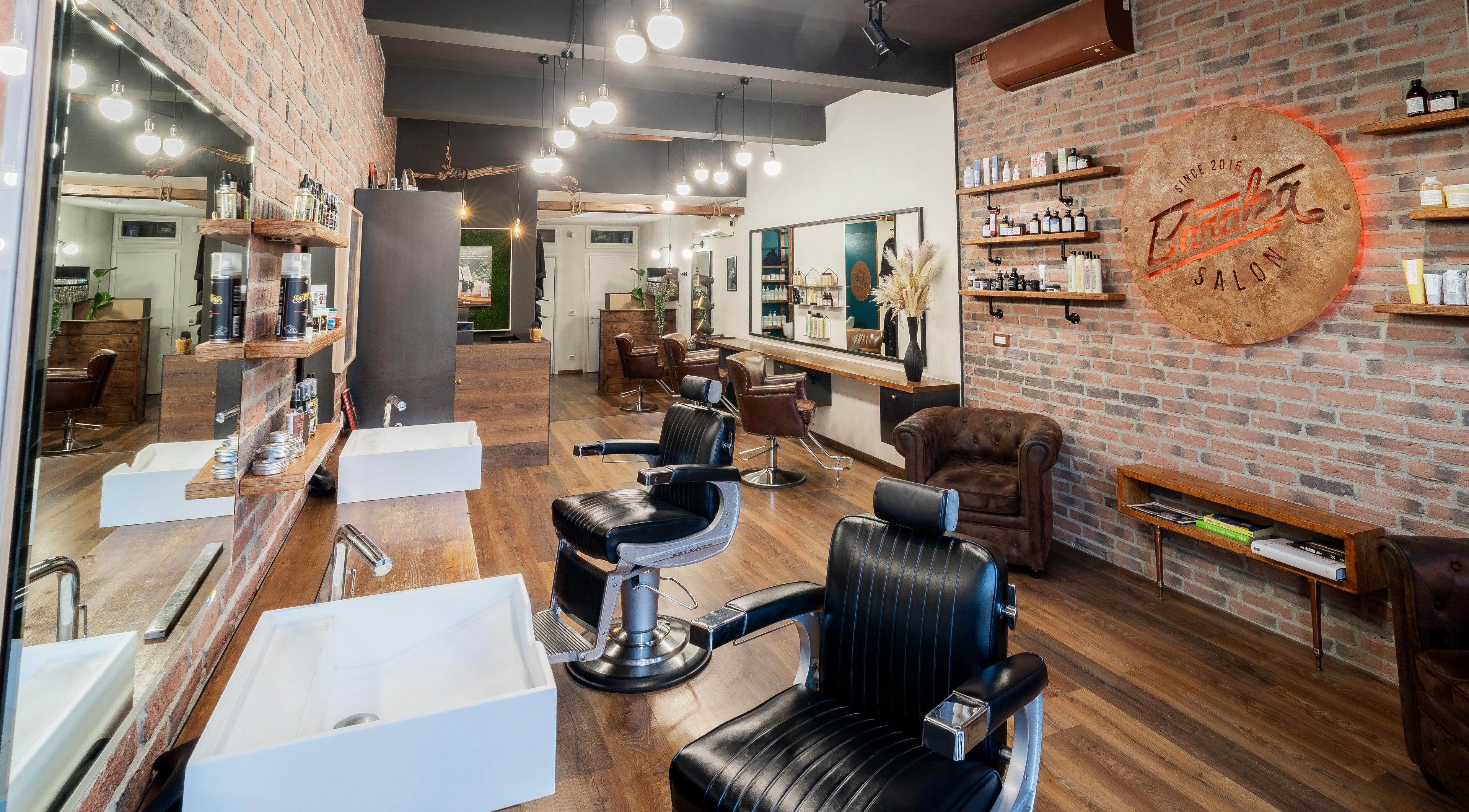 Interno moderno di Baraka Salon a Este, Veneto, IT con sedie da barbiere nere e pareti in mattoni.