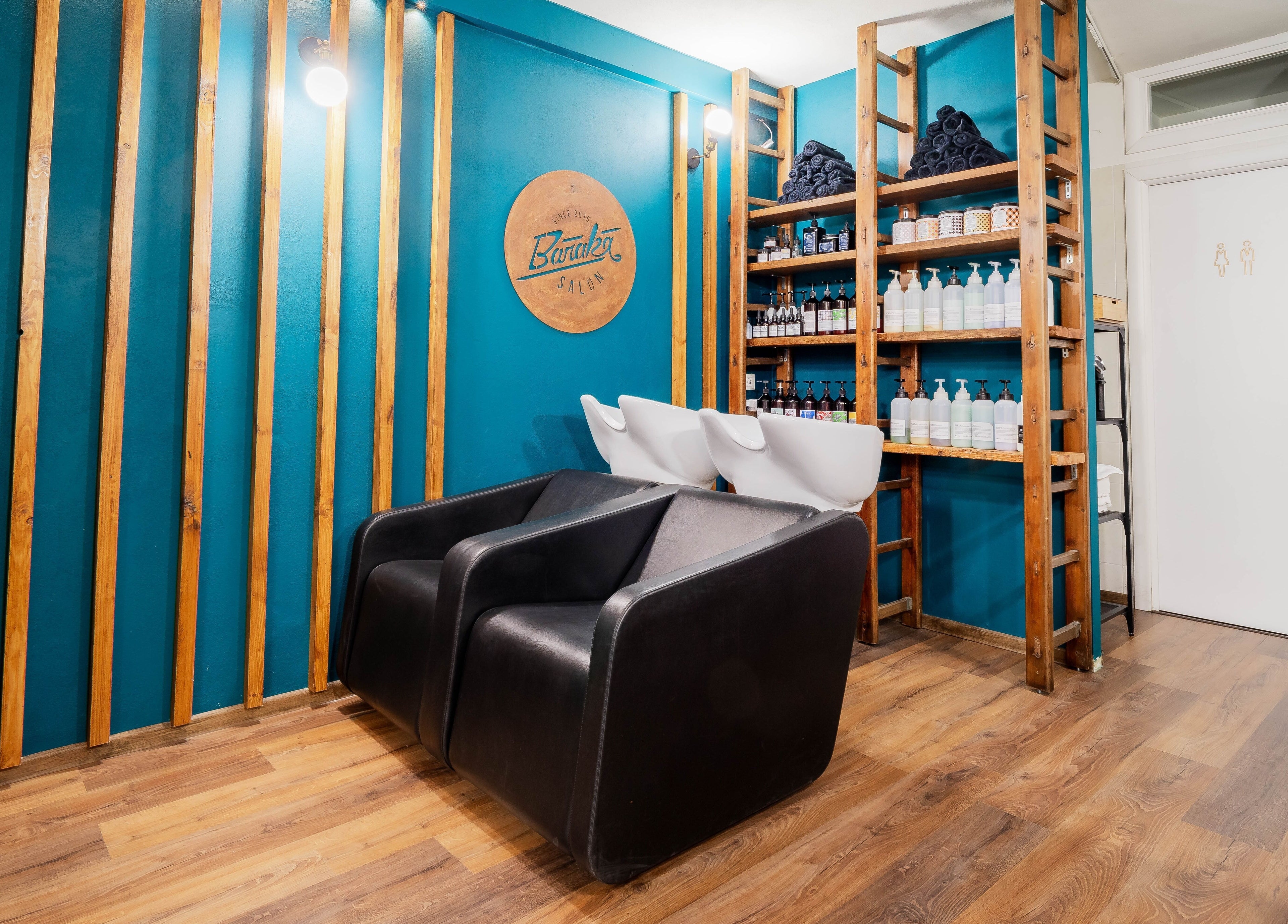 Interno di Baraka Salon, Este, Veneto, IT con poltrone nere e scaffali di prodotti.