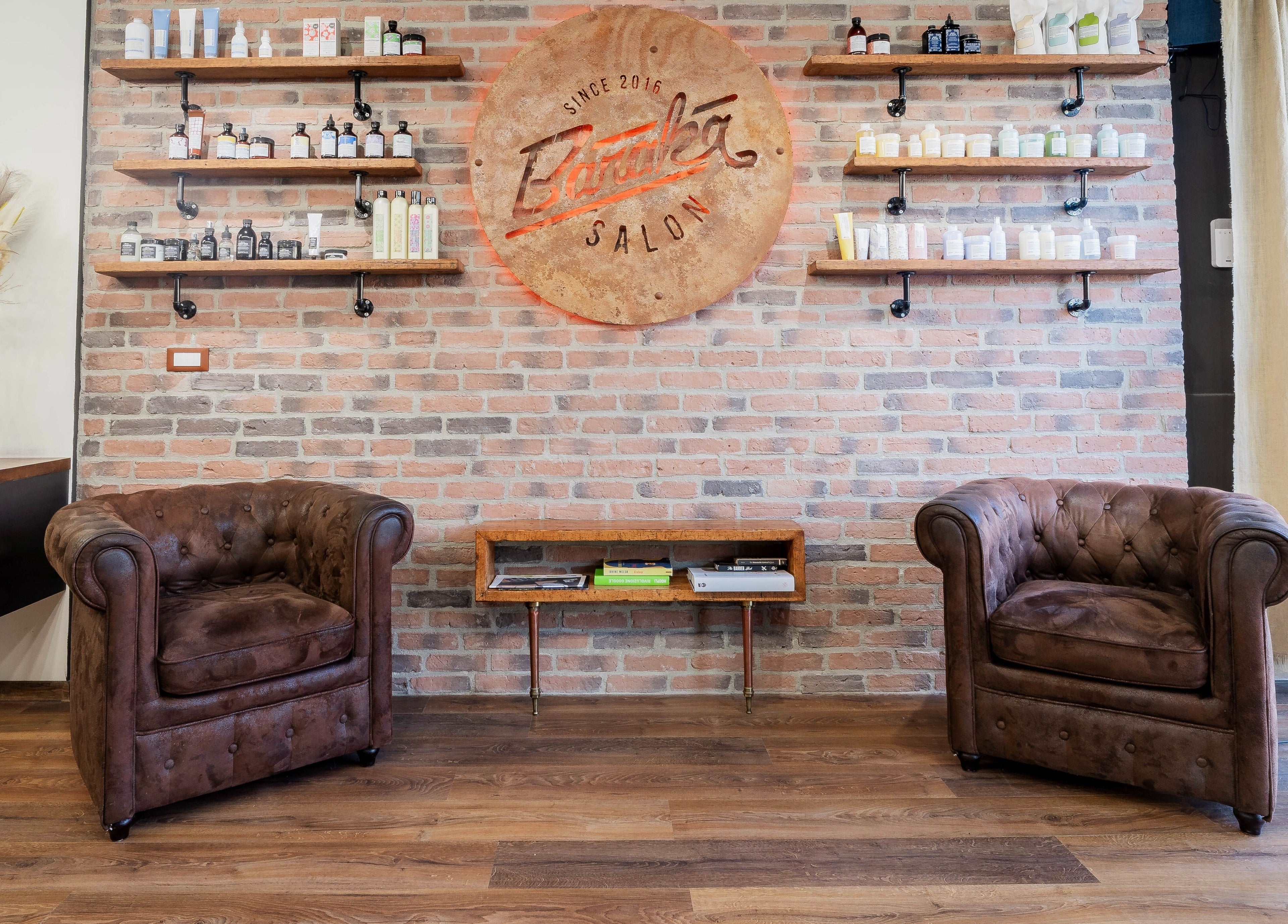 Interno Baraka Salon a Este, Veneto, IT con poltrone marroni e scaffali di prodotti di bellezza.