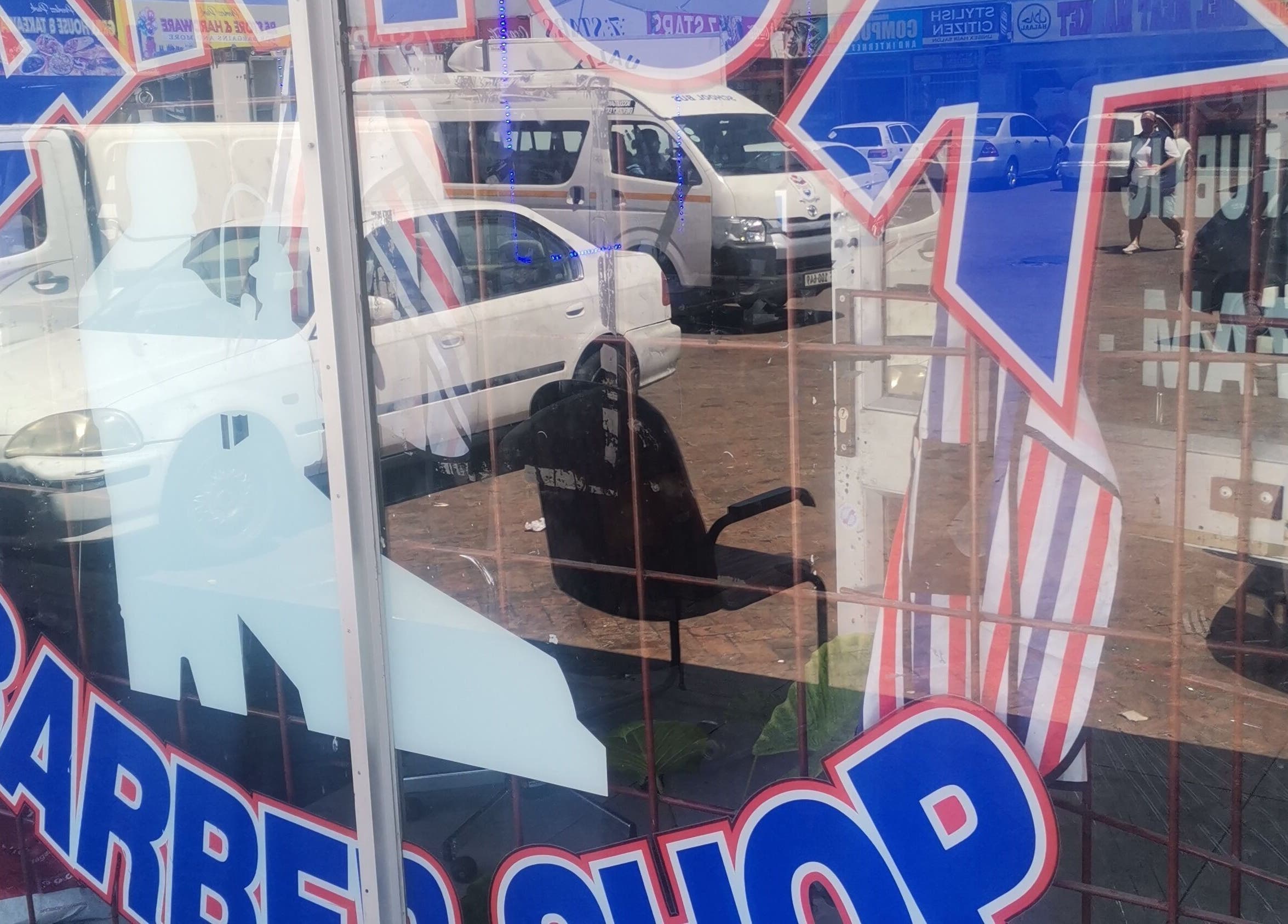 Street-facing barber shop window at C's_Cuts in Cape Town, Western Cape, ZA with a busy urban reflection.