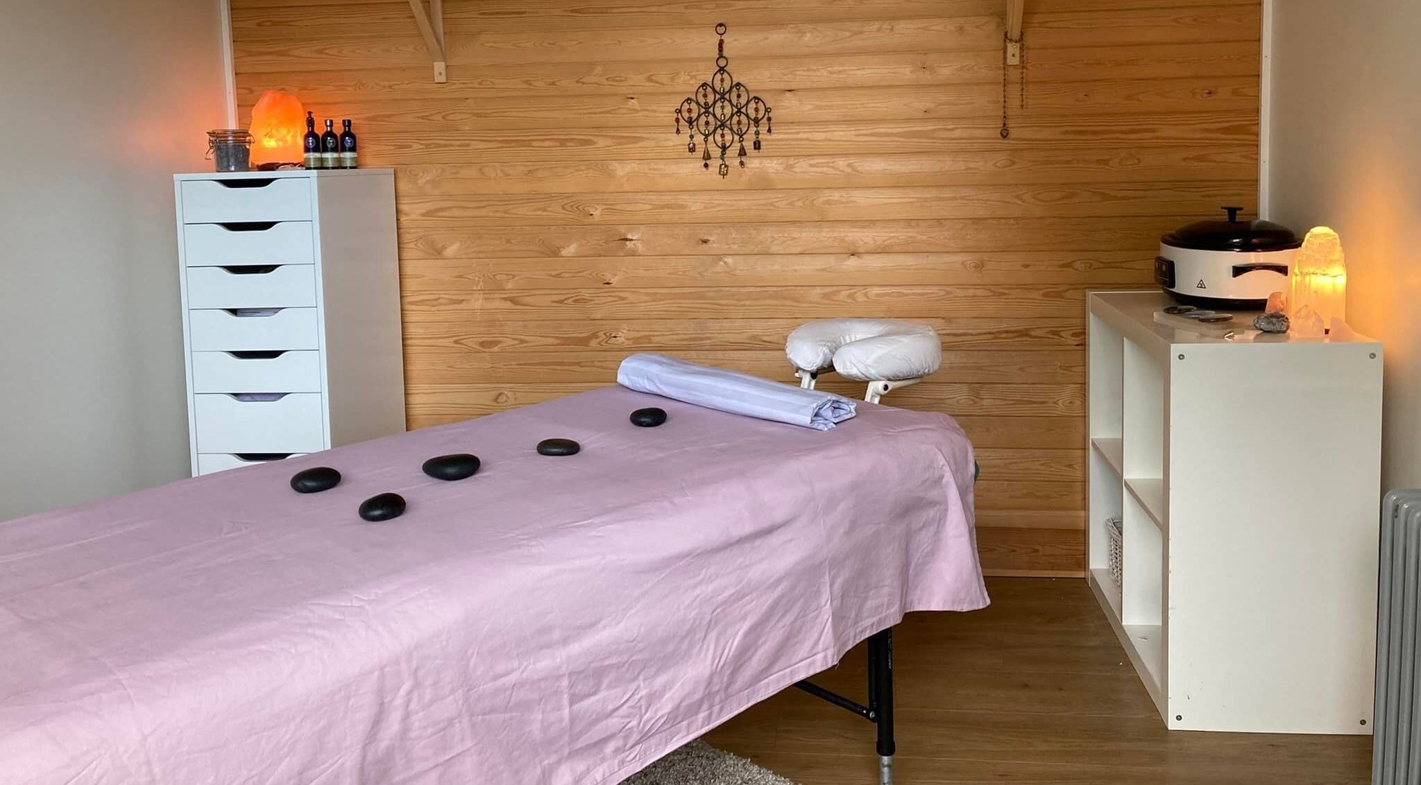 Peaceful massage room at Sue Hall, Saltford, England, GB, with table, stones, and warm lighting.