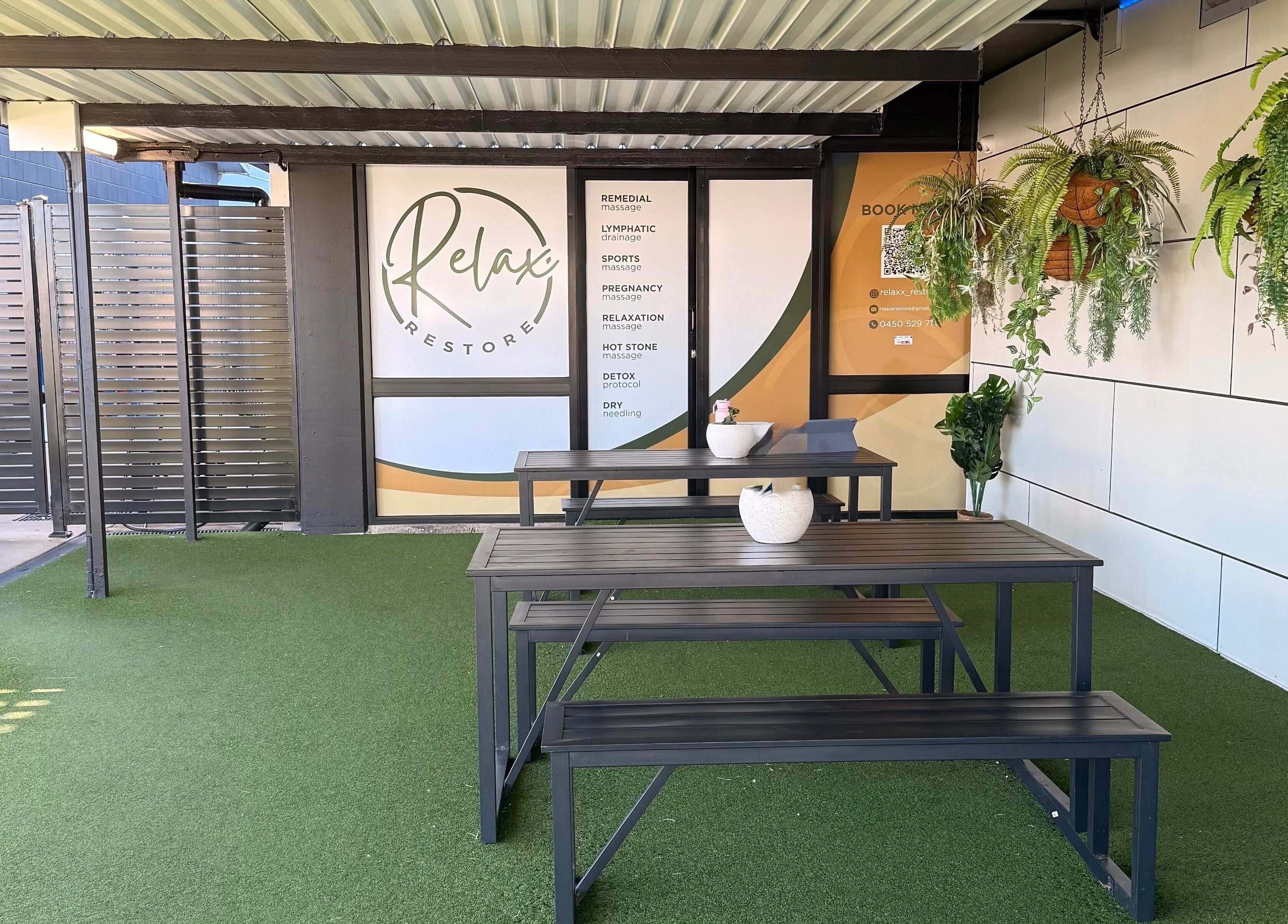 Outdoor seating area at Massage Relax Restore Townsville, Garbutt, Queensland, AU, featuring greenery and signage.