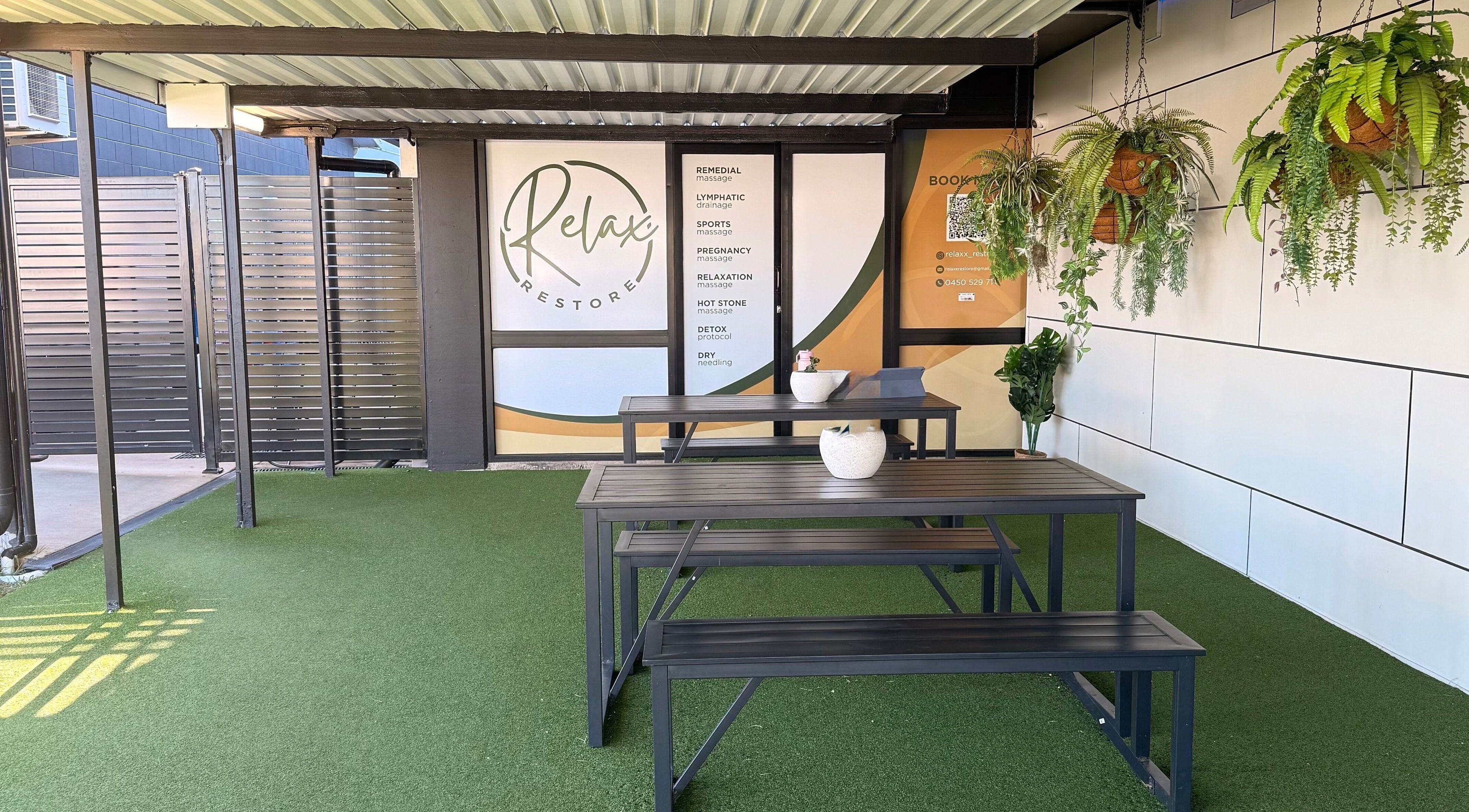 Outdoor seating area at Massage Relax Restore Townsville, Garbutt, Queensland, AU, featuring greenery and signage.