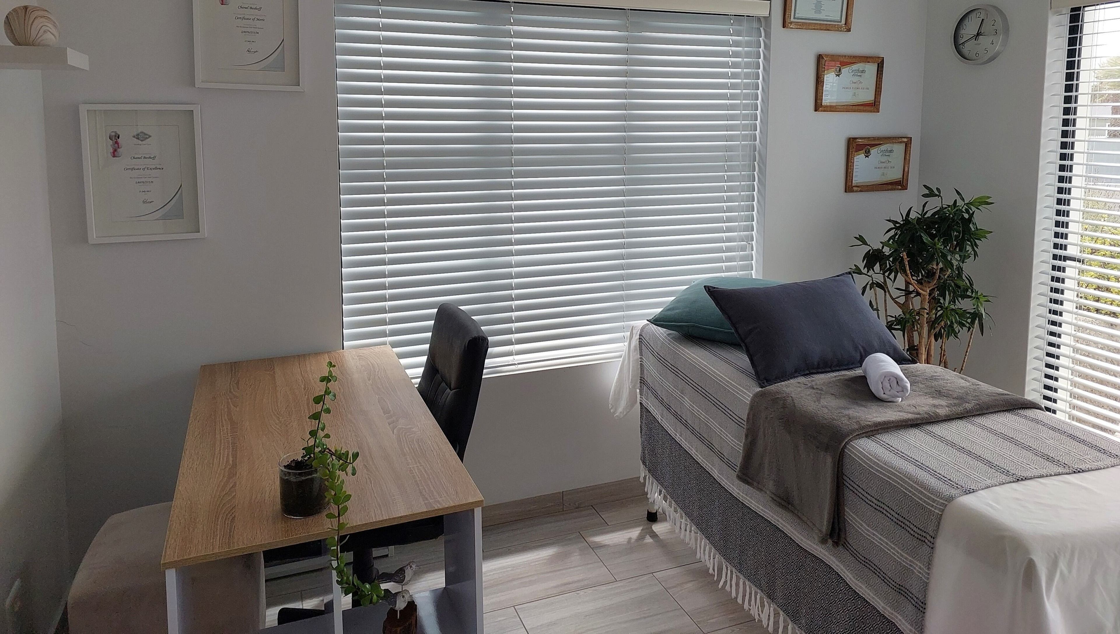 Calm treatment room at Blooms, Jeffreys Bay, Eastern Cape, ZA with a bed, desk, and plant for relaxation.