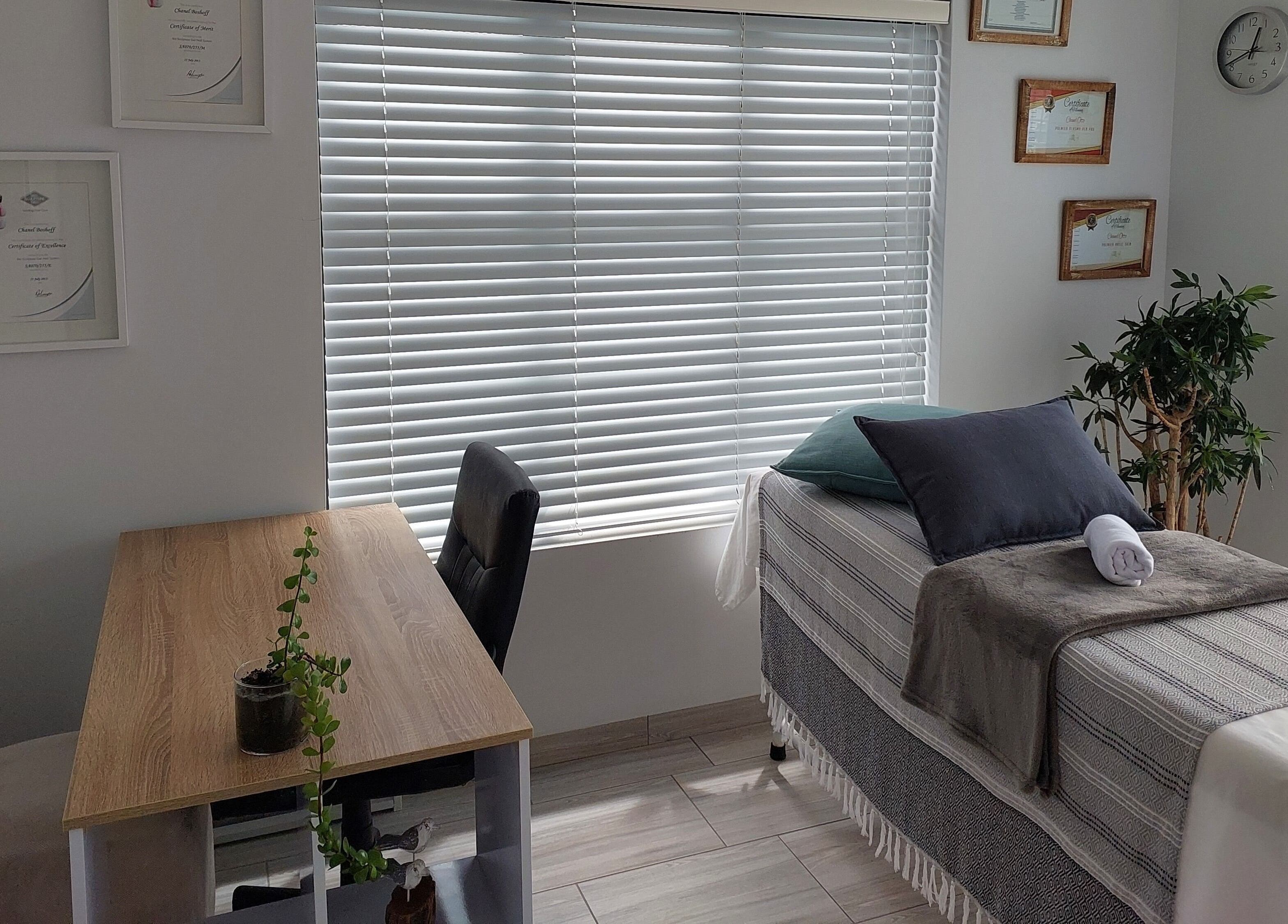 Calm treatment room at Blooms, Jeffreys Bay, Eastern Cape, ZA with a bed, desk, and plant for relaxation.