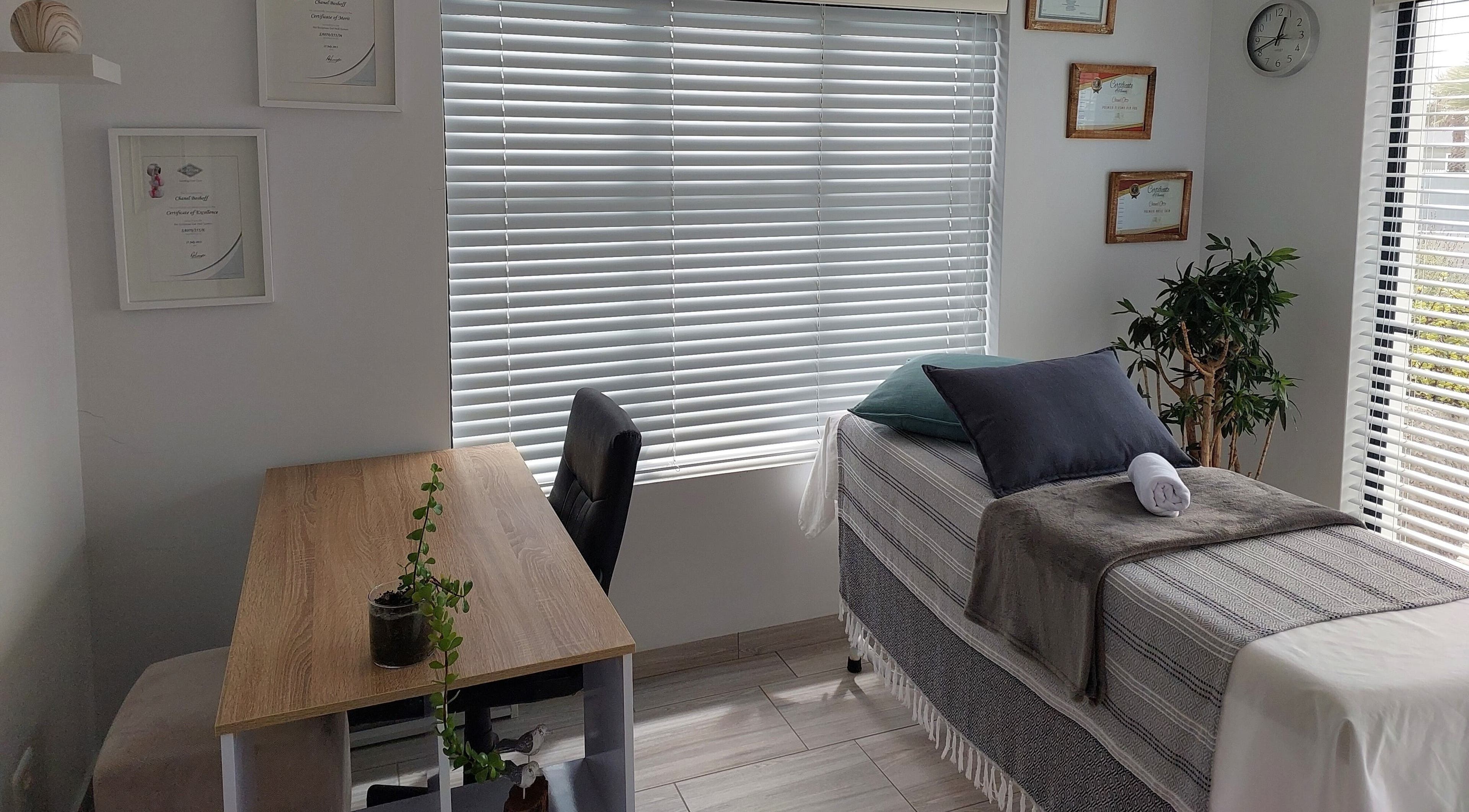 Calm treatment room at Blooms, Jeffreys Bay, Eastern Cape, ZA with a bed, desk, and plant for relaxation.