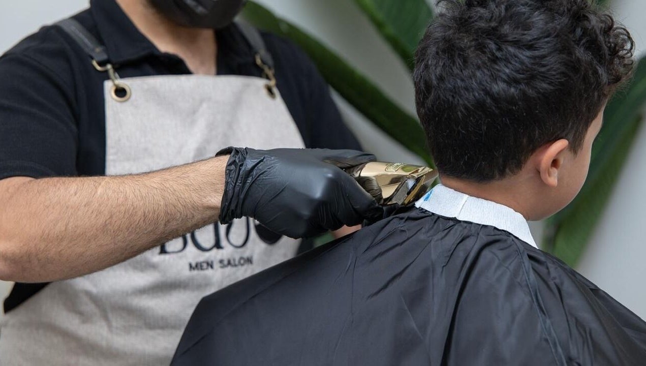 Barber giving a haircut at Lujo Barbershop, Al Khobar, Eastern Province, SA while wearing gloves.