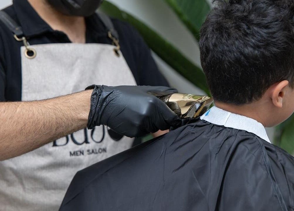 Barber giving a haircut at Lujo Barbershop, Al Khobar, Eastern Province, SA while wearing gloves.