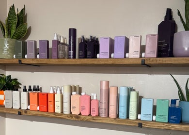 Two wooden shelves at South Beach Salon, Helston, England, GB, displaying various hair products and vibrant plants.