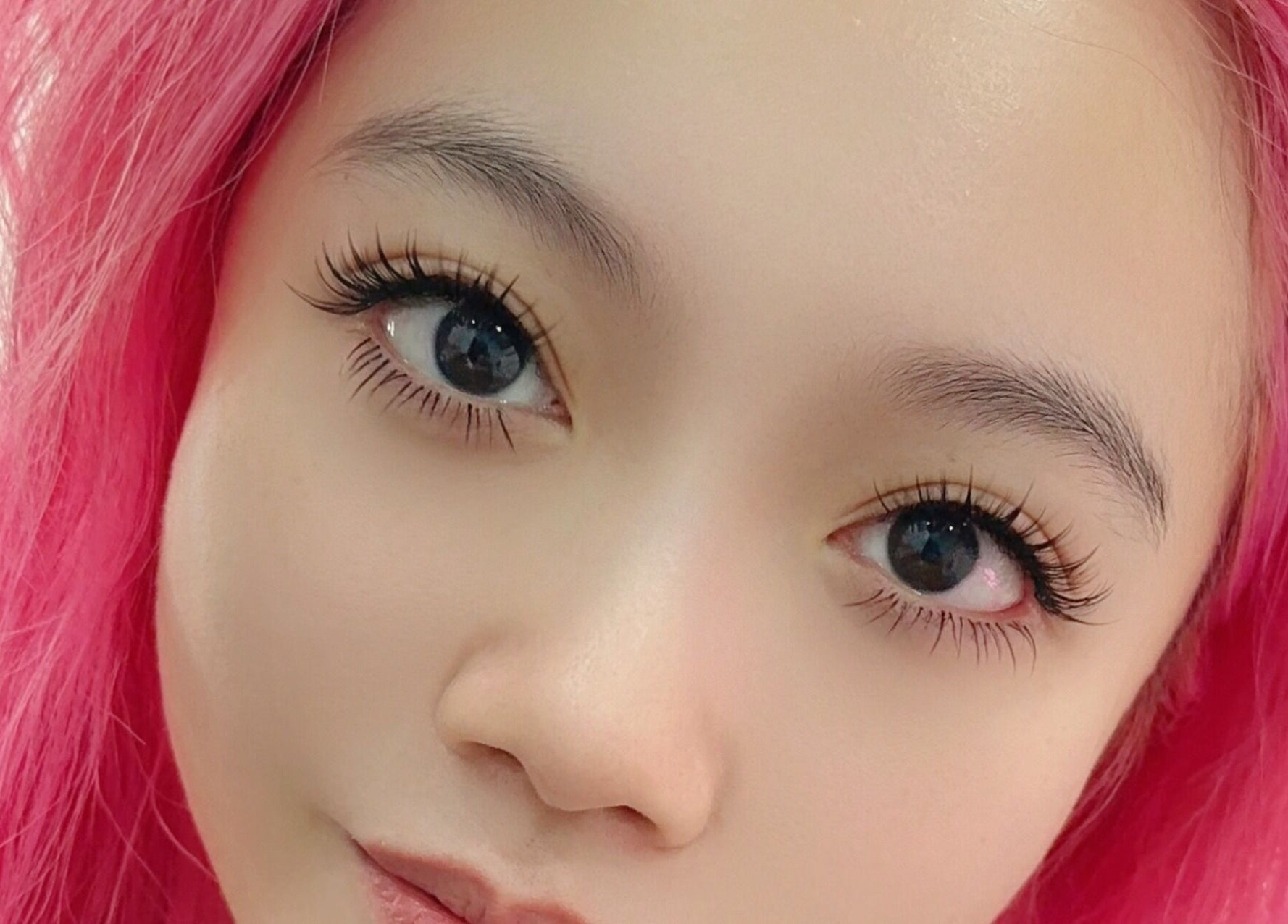 Close-up of a person with vibrant pink hair and enhanced eyelashes at Get Chio in Singapore, Singapore, SG.