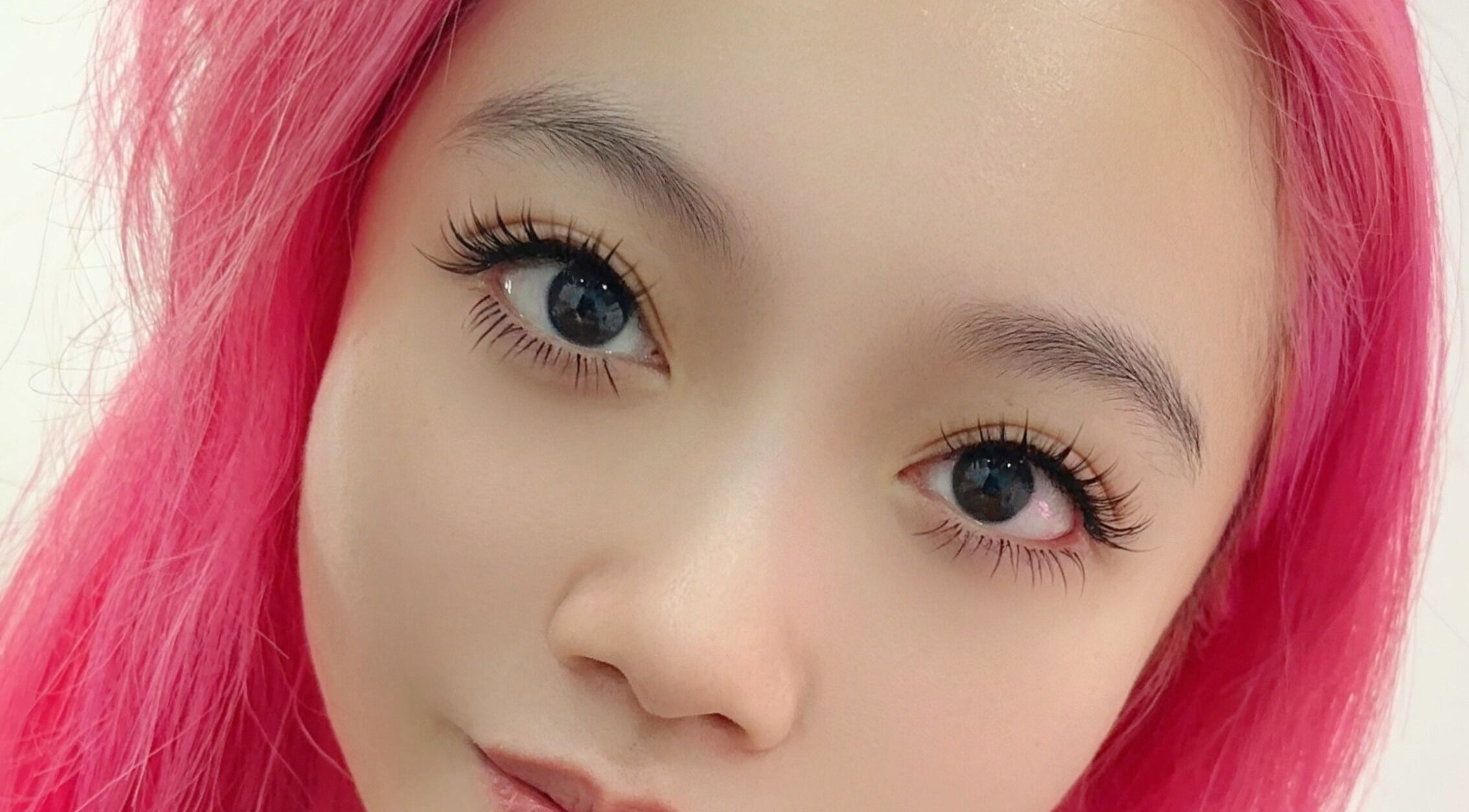 Close-up of a person with vibrant pink hair and enhanced eyelashes at Get Chio in Singapore, Singapore, SG.