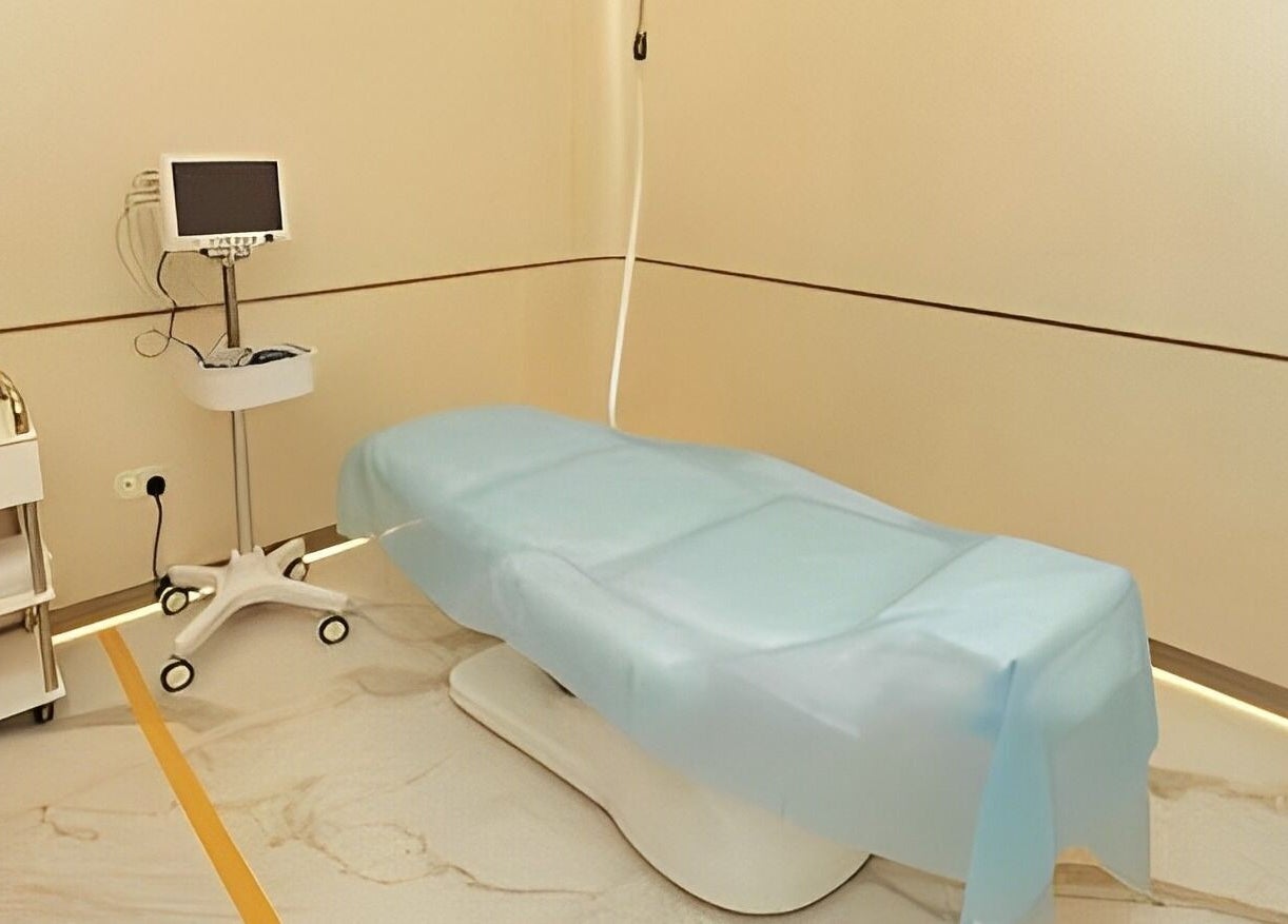 Modern treatment room at Reborn Clinic, Dubai, Dubai, AE, featuring a blue-covered medical bed and equipment.