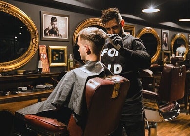 Barbero estilizando cabello en Masajes sdsd, Bilbao, ES, rodeado de espejos dorados.