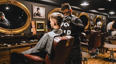 Barbero estilizando cabello en Masajes sdsd, Bilbao, ES, rodeado de espejos dorados.