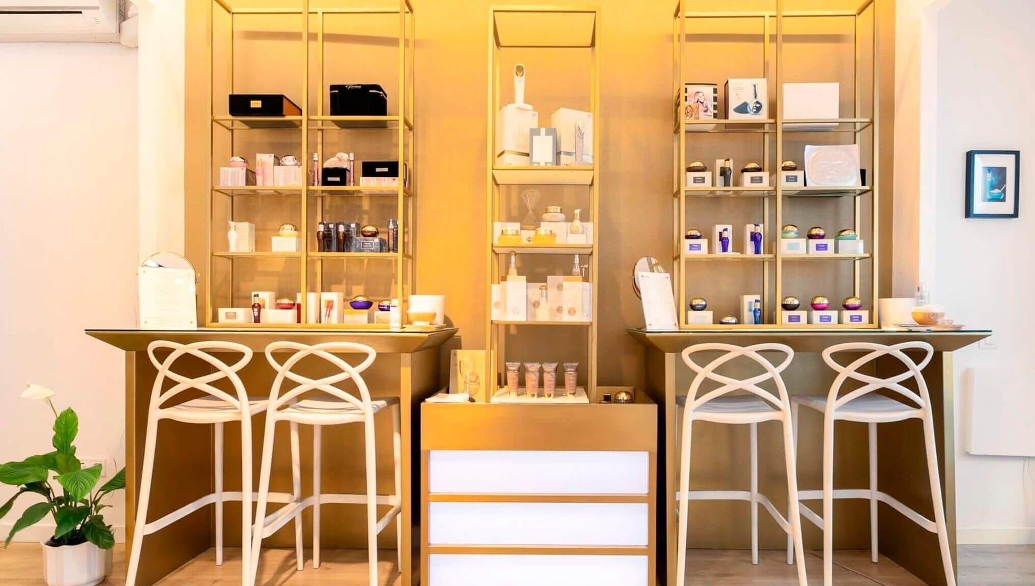 Estantería dorada con productos de belleza en Premier Sitges, Sitges, Catalunya, ES. Un ambiente elegante y moderno.