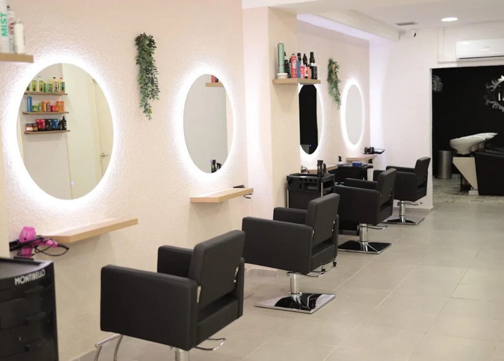 Elegante interior de Iria Perruquers en Cubelles, Catalunya, ES, con sillas negras y espejos iluminados.