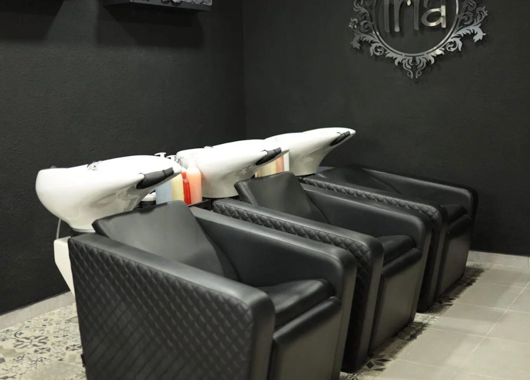 Zona de lavado moderna en Iria Perruquers, Cubelles, Catalunya, ES, con sillones negros y fregaderos blancos.