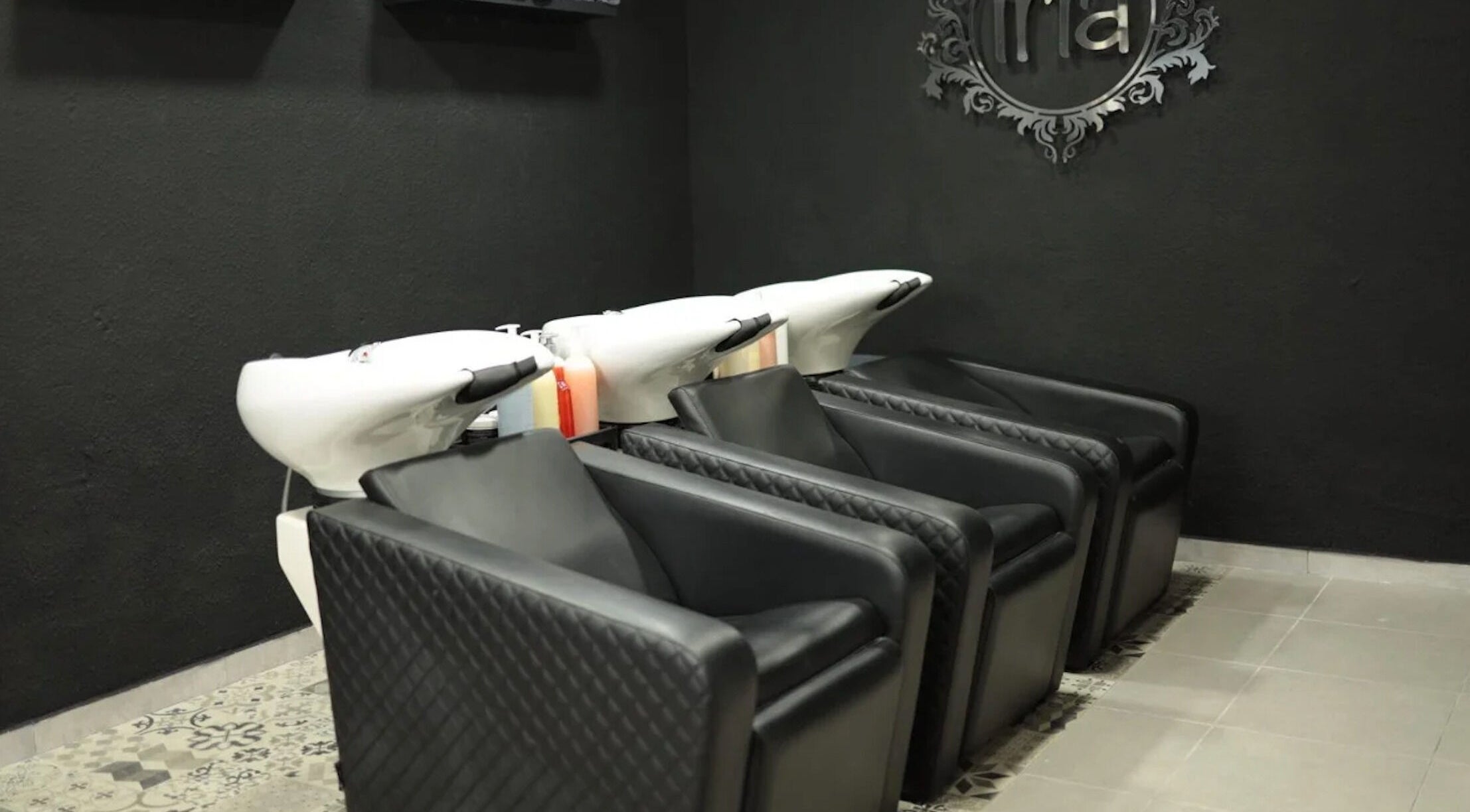 Zona de lavado moderna en Iria Perruquers, Cubelles, Catalunya, ES, con sillones negros y fregaderos blancos.