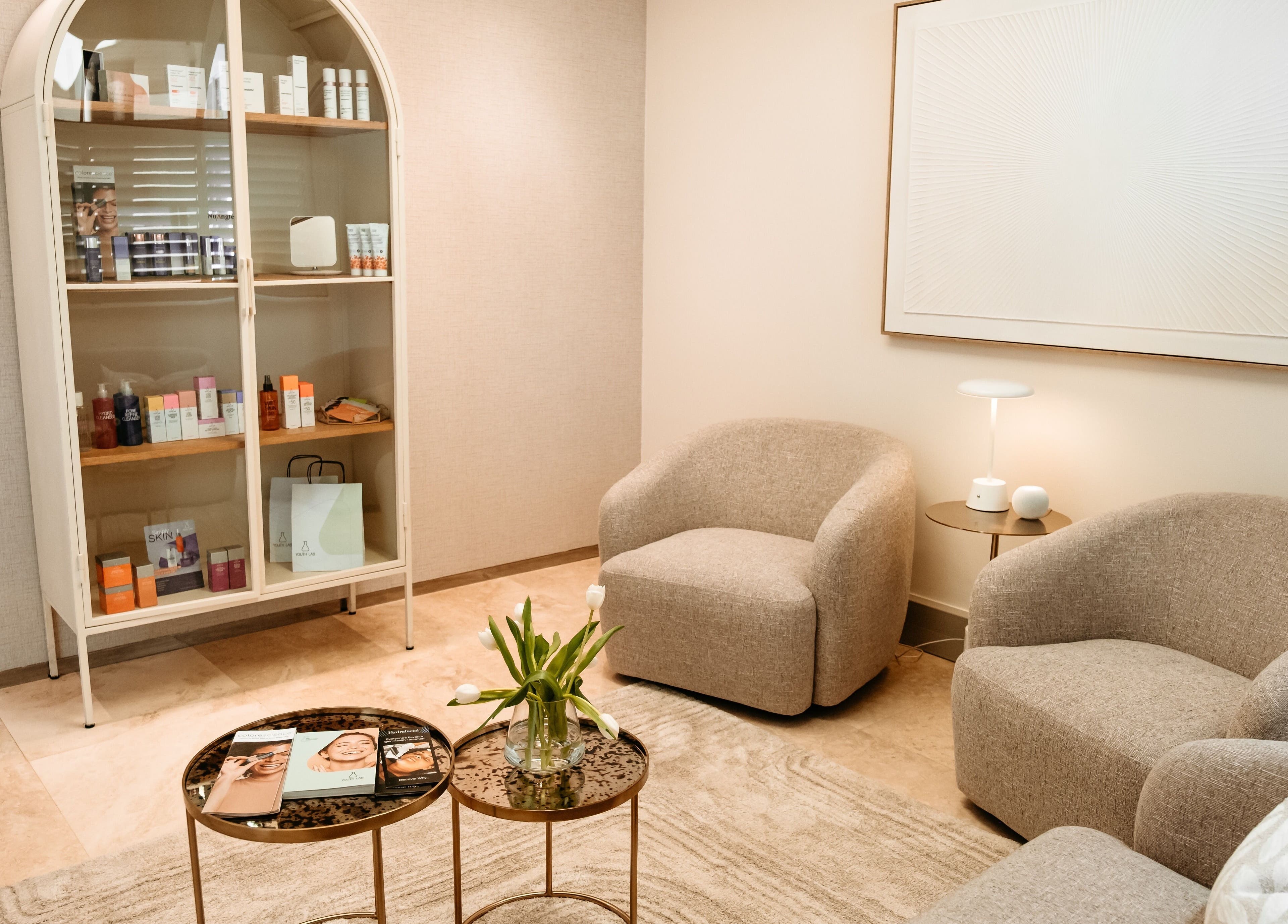 Cozy lounge at The Dermal Collection, Cape Town, Western Cape, ZA with elegant chairs and a display cabinet.