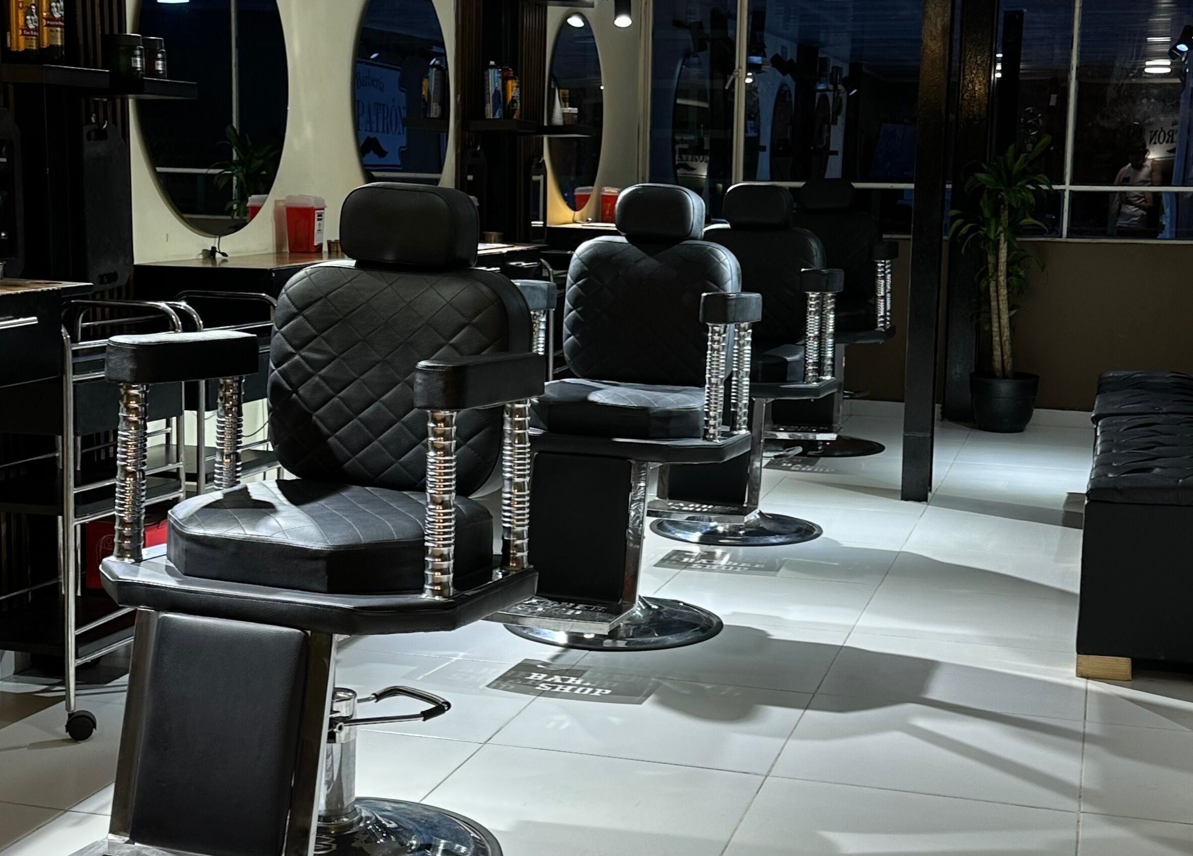Interior de EL PATRÓN barbería en Soacha, Cundinamarca, CO con elegantes sillas negras y espejos iluminados.