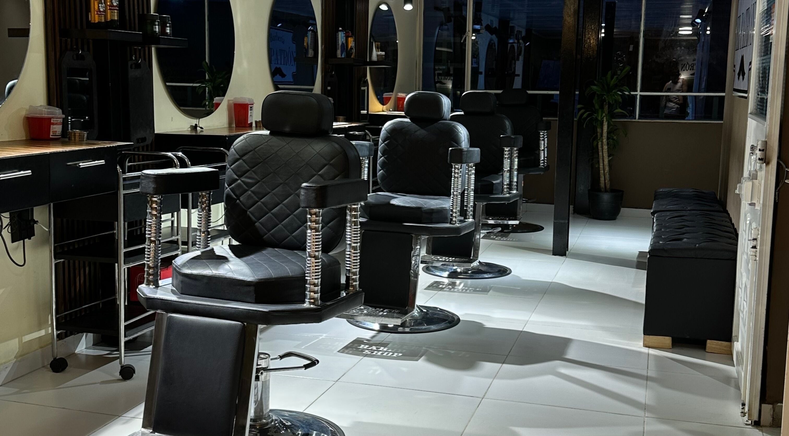 Interior de EL PATRÓN barbería en Soacha, Cundinamarca, CO con elegantes sillas negras y espejos iluminados.