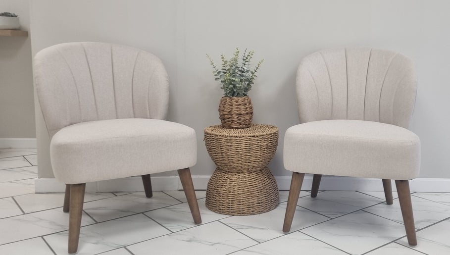 Stylish seating at Brow & Beauty in Mansfield, England, GB. Features two beige chairs and a wicker table with plant.