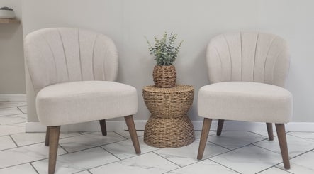 Stylish seating at Brow & Beauty in Mansfield, England, GB. Features two beige chairs and a wicker table with plant.