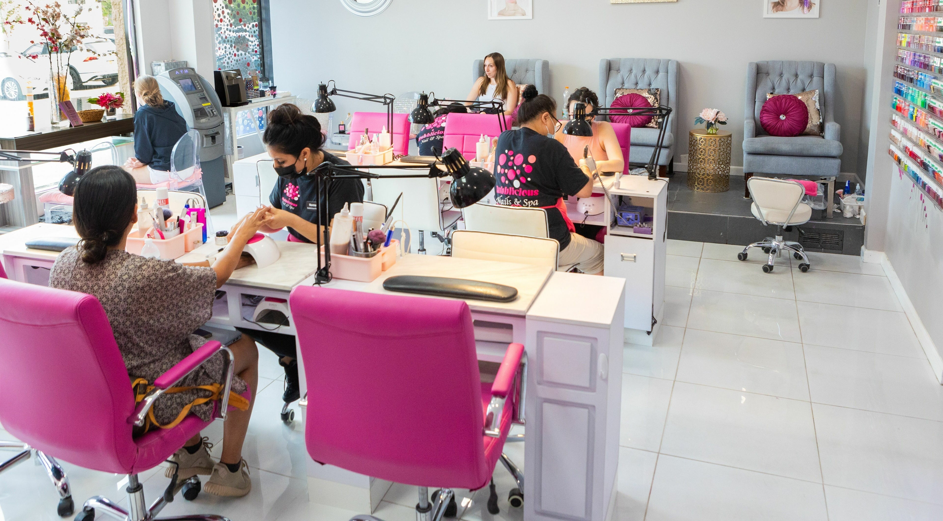 Manicure session at Bubblicious Nails and Spa, New York, New York, US with vibrant pink chairs and nail polish display.
