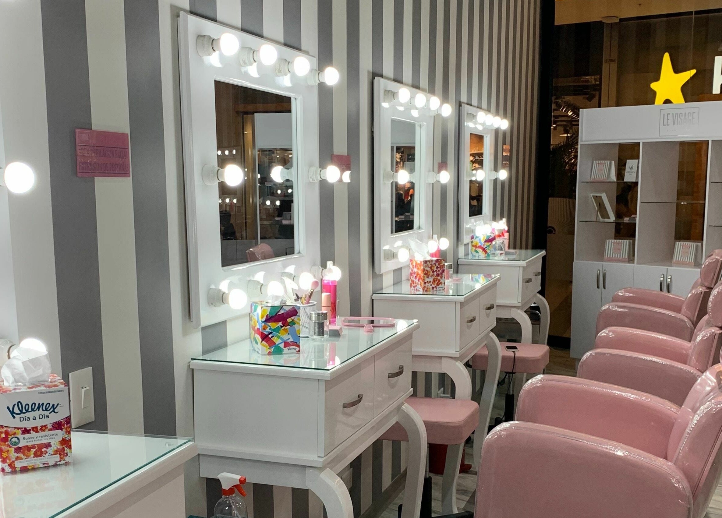 Elegantes estaciones de belleza en Le Visage Parque la Colina, Bogotá, CO con sillas rosas y espejos con luces.