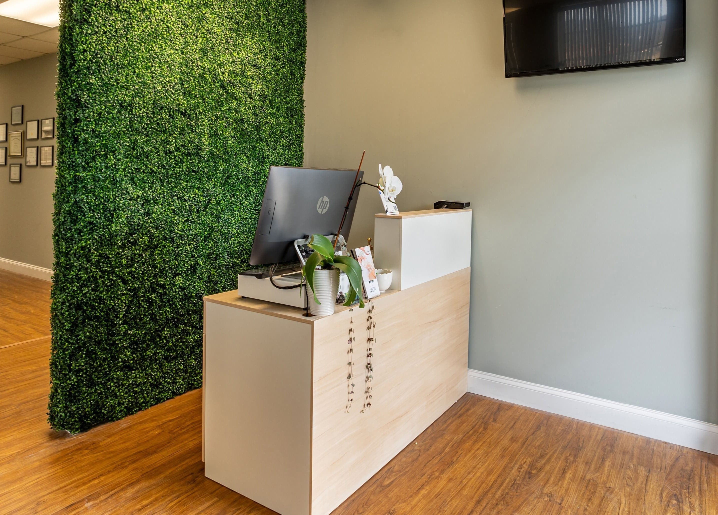 Reception desk at BEAUTYOLOGY, Ooltewah, Tennessee, US, with greenery and wood floor, exuding warmth.