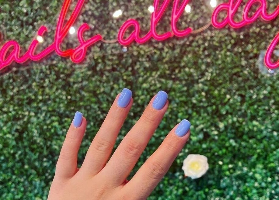 Hand with blue nails at NailBar Studio in Naperville, IL, US with neon sign backdrop.