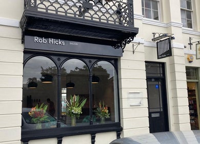 Exterior of Rob Hicks Salon in Cheltenham, England, GB featuring stylish black accents and floral displays.