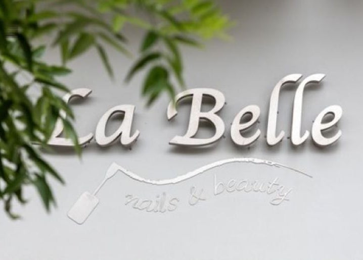 Λογότυπο της La Belle, Καλαμαριά, GR, με φυλλώματα στο φόντο.