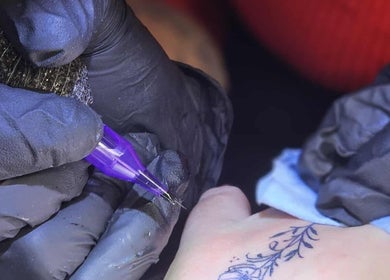 Tattoo artist at She Studios, London, Ontario, CA creating a floral design on a client's hand.