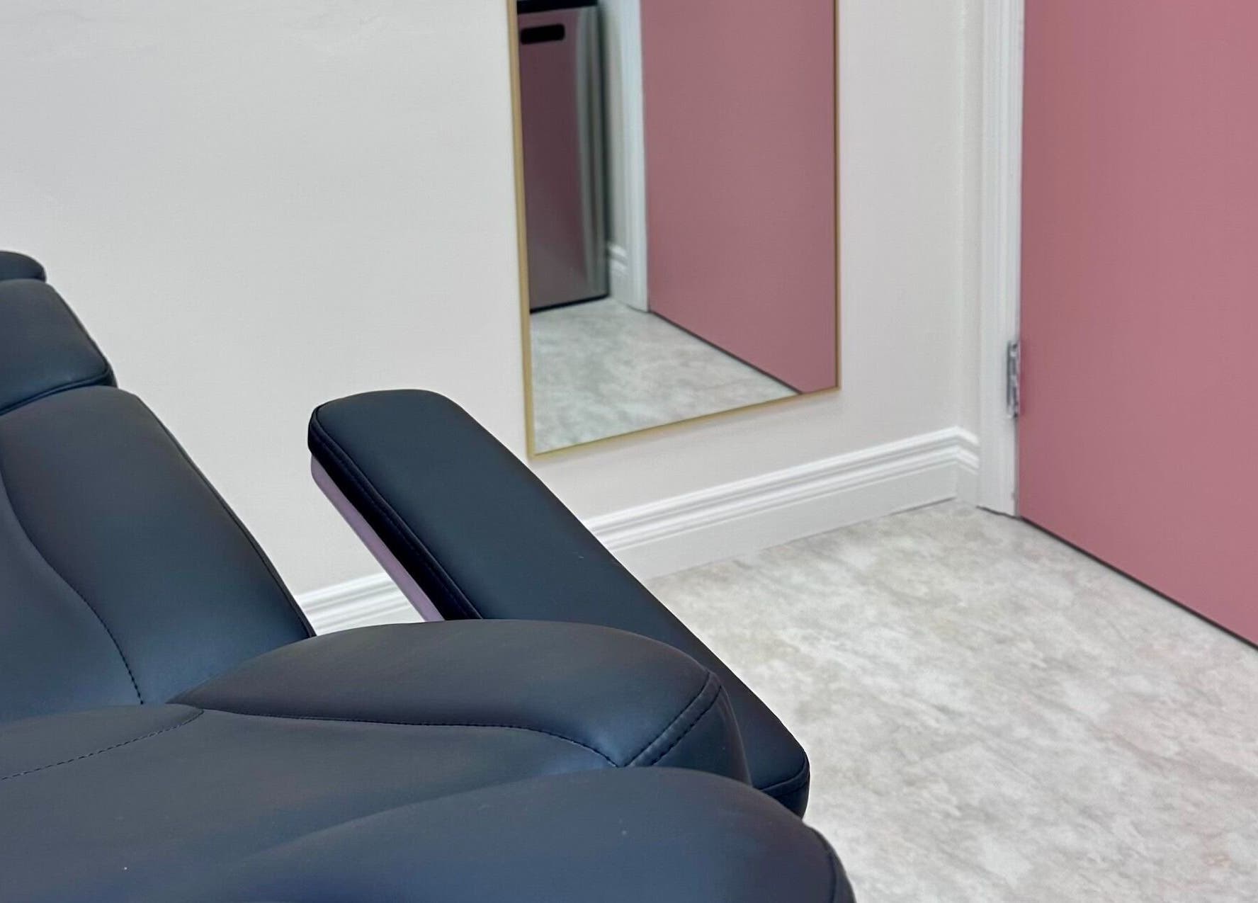 Modern treatment room at Pretty Hurts in Leduc, Alberta, CA, featuring sleek black seating and pink accents.