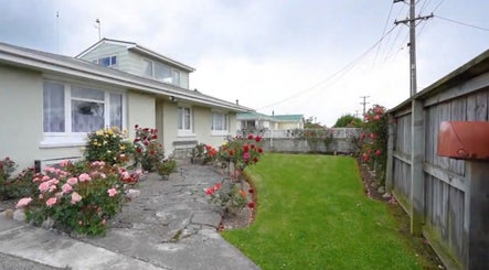 Charming garden exterior of JNT Nails in Invercargill, Southland, NZ, featuring blooming roses and lush greenery.