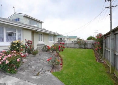 Charming exterior of JNT Nails in Invercargill, Southland, NZ, featuring colorful roses and lush greenery.