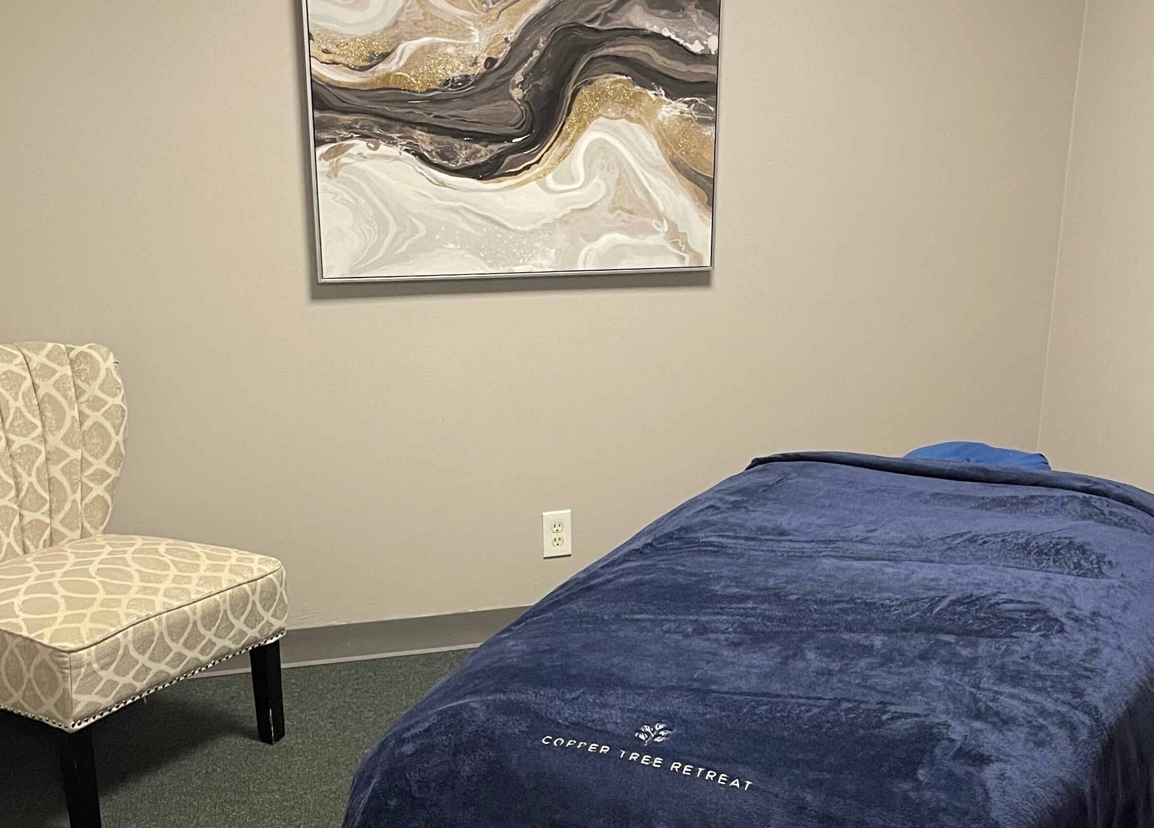 Relaxing massage room at Copper Tree Retreat, Longview, Texas, US, featuring cozy chair and elegant artwork.