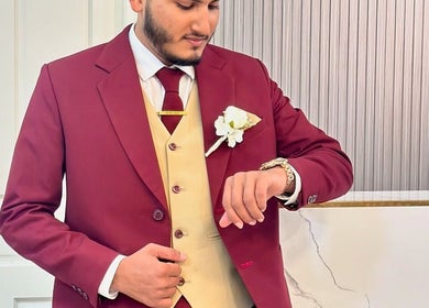 Person in burgundy suit with flower pin at Gloss Salon, Malé, Male, MV checking watch.